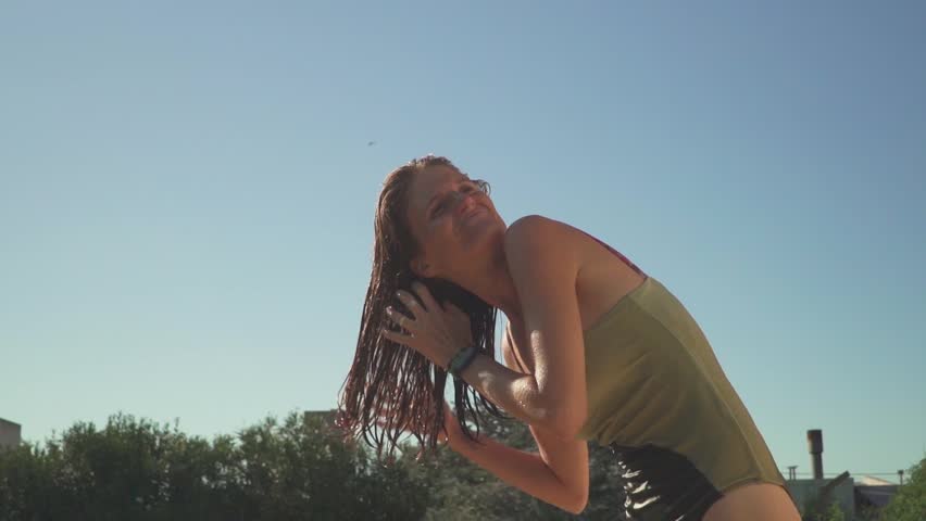 View of a young woman in a swimsuit brushing her wet hair by hand. Low-angle, slow-motion.
