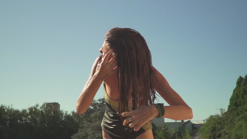 View of a young woman in a swimsuit brushing her wet hair by hand. Low-angle, slow-motion.