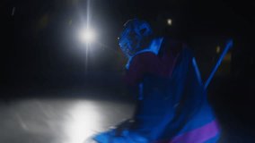 Ice hockey goalie goaltender warms up before game Workout butterfly drill exercise. Goalkeeper stretches his legs at goal. Protective gear equipment. Blue light. Ice arena with lights off - Powered by Shutterstock - Get 15% off with code: PIKWIZARD15