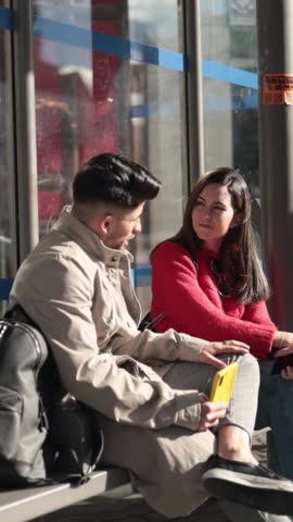 Young man and woman talking and waiting at the bus stop. Real friendship concept.