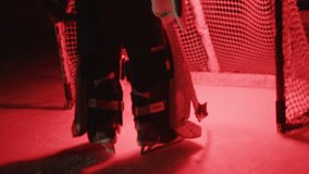 Close up Ice hockey goalie goaltender warms up before game Workout drill exercise. Goalkeeper stands at goal. Protective gear equipment. Red light. Dark Ice arena with lights off. Handheld shaky shot - Powered by Shutterstock - Get 15% off with code: PIKWIZARD15