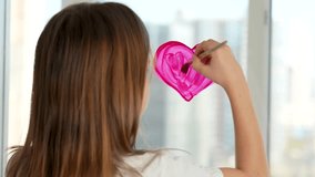 Cute girl painting heart on window with paintbrush, close-up, Little girl painting red heart with paintbrush and red paint on glass surface