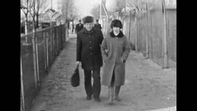 Man, woman portraits in winter clothes, fur hats on street. Adult married couple walk along city outdoors in coats in cold autumn. Nordic 80s fashion. Vintage black white film. archive. Retro 1980s