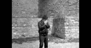 Stylish adult man lighting cigarette on city street. Man in hat, leather jacket smoking cigarette. Harmful, bad health habit. Archival vintage black white film. Old retro archive. 1980s Crimea