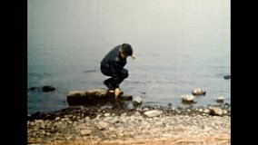 Adult man on calm sea backdrop in autumn. Stylish man in hat black leather jacket resting near water in spring. Relaxation on marine nature. Archival vintage color film. Old retro archive 1980s Crimea