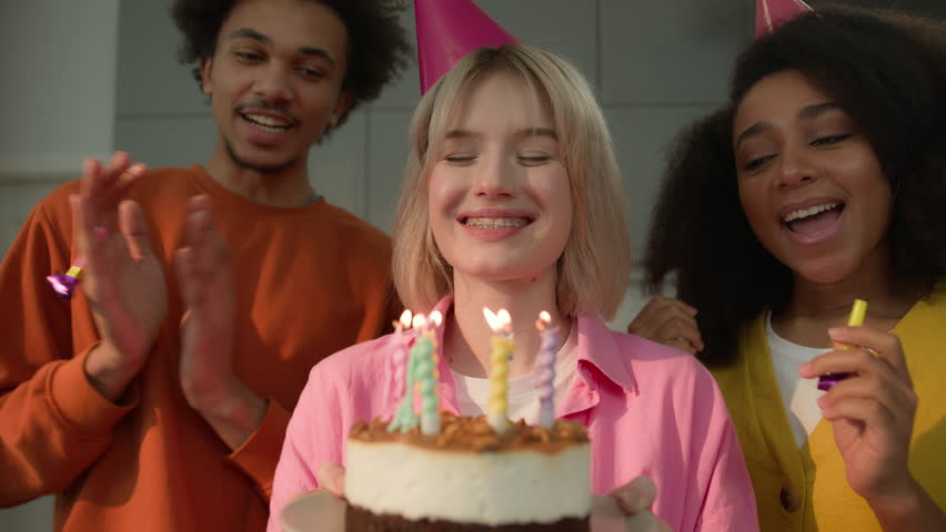 Birthday party group happy multiracial people at home joyful multiethnic friends diverse women man girls together celebrate birth girl woman in festive hat blow cake with candle wish celebration event