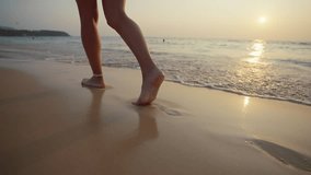 Woman feet barefoot on beach close up. Female tourist running on the beach by sea ocean, enjoying the sunrise. Close up of legs and feet in the sea water. Travel, tourism, outdoors vacation concept.