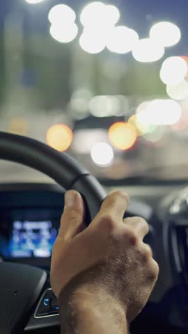 Man hands on steering wheel. Driving car in evening city through traffic jam. Driving car through the night city. City traffic and lights. Vertical shot
