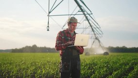 corn agriculture. male farmer works on a laptop in a field with green corn sprouts. corn is watered by irrigation machine. irrigation agriculture business sunlight concept - Powered by Shutterstock - Get 15% off with code: PIKWIZARD15