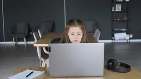 A young girl puts on wireless headphones while sitting in front of a laptop and doing online learning. Close-up.