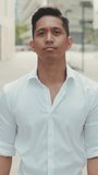 VERTICAL VIDEO: Young businessman looking at the camera while standing in the business district
