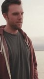 VERTICAL VIDEO: Young man talking while standing on seascape