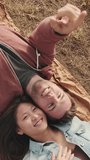 VERTICAL VIDEO: Young couple lying on blanket in the park from outside