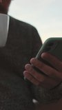 Vertical video, Close-up of the hands of guy standing on the balcony drinking coffee from mug, browsing the web on smartphone
