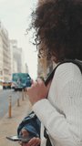 Vertical video, Young woman tourist is waiting for a taxi. Girl with a backpack stands next to the road waiting for a taxi