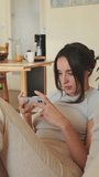 VERTICAL VIDEO, Young woman using mobile phone while sitting on sofa at home
