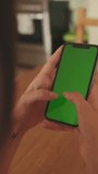 VERTICAL VIDEO, Close-up of young woman's hands using mobile phone green screen chroma key at home