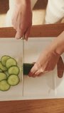 VERTICAL VIDEO, Close-up of young woman's hands cutting cucumbers making salad at home in the kitchen. View from above
