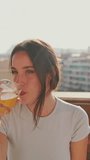 VERTICAL VIDEO, Young woman sits on the balcony in the house and drinks juice