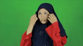 Asian Muslim teenager straightens her hijab. Arranging clothes on green background studio - Powered by Shutterstock - Get 15% off with code: PIKWIZARD15