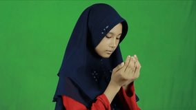 A young woman in a hijab and reading a prayer on a green background. Asian child in hijab praying to Allah. Ask God for guidance - Powered by Shutterstock - Get 15% off with code: PIKWIZARD15