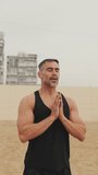 Vertical video, Athletic mature man doing relaxing breathing exercises standing in the morning on the beach