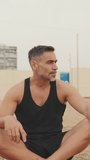Vertical video, Middle aged athletic man relaxing after workout while sitting in lotus position on the beach
