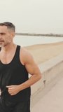 Vertical video, Middle-aged muscular man runs along the promenade before jogging