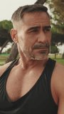 Vertical video, Close up, middle aged muscular man relaxing after workout while sitting in park outdoors