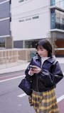 Vertical video of a young Japanese woman in her 20s walking around Gotanda Station, Shinagawa-ku, Tokyo with a smartphone in winter