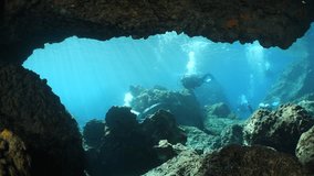  scuba divers exploring topography and   reefs underwater deep blue water big rocks and bubbles ocean scenery 