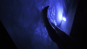 Vertical video of woman moving legs underwater pool illuminated by blue light at night 