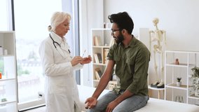 Confident mature woman in lab coat holding syringe with seasonal flu vaccine while young man sitting in exam room. General practitioner giving injection to boost immunity for young bearded patient. - Powered by Shutterstock - Get 15% off with code: PIKWIZARD15
