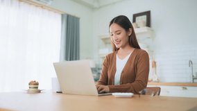 Beautiful young Asian woman working with laptop computer in home kitchen. Work at home - Powered by Shutterstock - Get 15% off with code: PIKWIZARD15