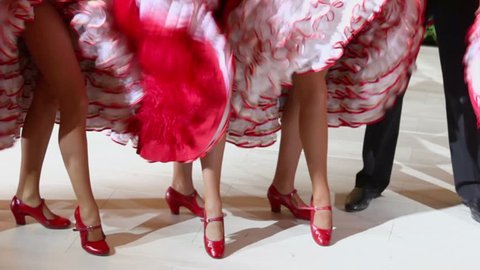Cancan dancers stand and shake dresses near men in black pants, closeup view with only legs visible