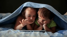 Little boy and girl play on the tablet while lying under a blanket. High quality 4k footage