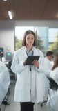 Vertical Screen: Female Scientist Posing for Camera, Smiling. Young Biologist Standing in a White Coat, Using a Tablet Computer in a Modern Laboratory, Researching Pharmaceutical Products