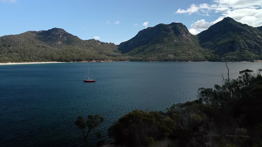 Profile view of hills of Freycinet National Park with a boat sailing on a lake at foreground in Tasmania, Australia. Drone view.