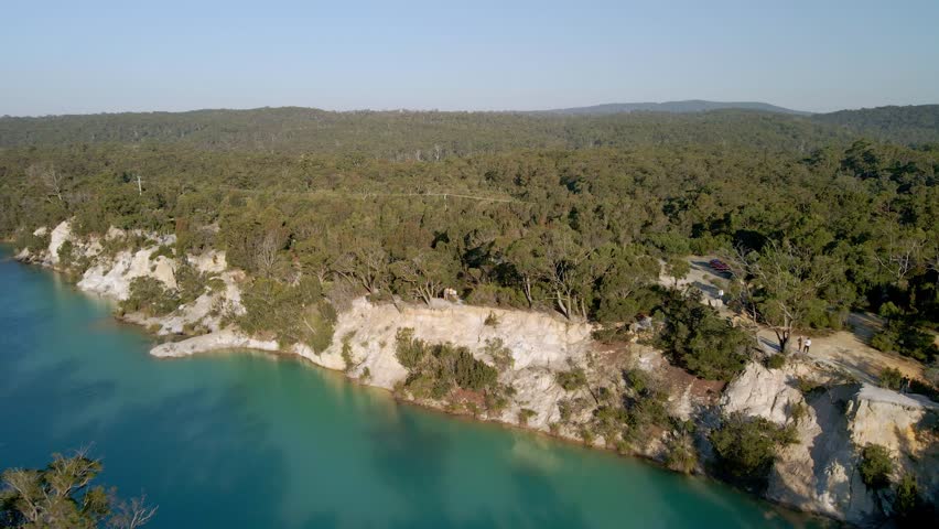 Backward drone shot of turquoise little lake in between a dense forest in Tasmania, Australia. 