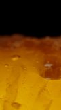 Vertical video. Honey being poured onto golden honeycombs against a black background. Macro Dolly