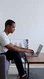 Vertical HD video. Side view of young millennial student working on laptop sitting on sofa at home. Technology and education concept. Copy space for text on the wall.