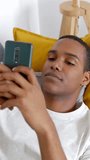 Vertical HD video. Young adult man using mobile phone on the sofa. Happy millennial male chatting on smartphone app relaxing at home. Technology lifestyle concept.