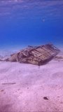 Vertical video, Camera moving forwards approaching to discarded old sofa lying on sandy bottom on shallow water in sun glare, Mediterranean sea, Slow motion. Concept pollution of Ocean