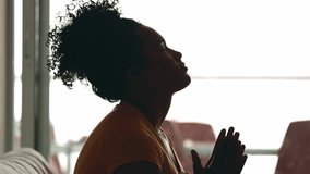 Silhouette profile of a young black woman PRAYING to GOD at home, 20s person pleading for HELP and SUPPORT during challenging times, having HOPE and FAITH - Powered by Shutterstock - Get 15% off with code: PIKWIZARD15