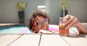 A young biracial man relaxes in a pool at home. He has curly hair, sports sunglasses, and rests on a colorful float, unaltered, slow motion.