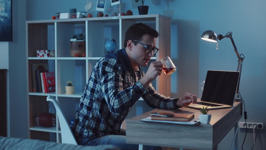Attractive office worker working hard at his cabinet late at night, drinks tea and programming something on his computer. Workaholic, freelance position, making money. Slow motion, camera stabilizer | Shutterstock HD Video #34773088