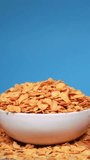 Slow motion of pouring crispy common cornflakes or cereals into a bowl. Cornflakes falling down against blue background. Organic breakfast, healthy lifestyle, vegetarian diet concept.