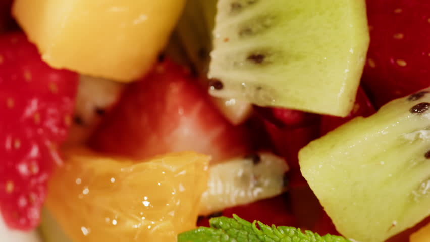 Health fresh colorful fruit salad with kiwi, orange, strawberries, mango, banana and mint on the top in bowl on table close-up macro. Healthy vegan detox summer recipe. Food concept