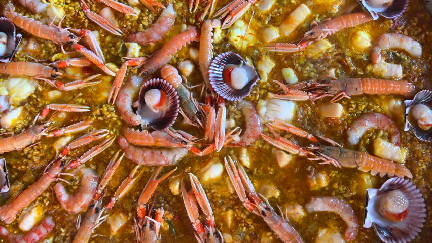 Cooking a big traditional Spanish seafood Paella dish with shrimps, St Jacques scallops and Cigala Norway lobsters Nephrops norvegicus, tasty cooked rice with seafood, Marbella Spain, 4K shot
