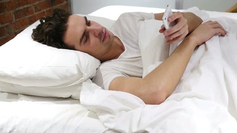 Man in Bed Browsing on Smartphone at Night